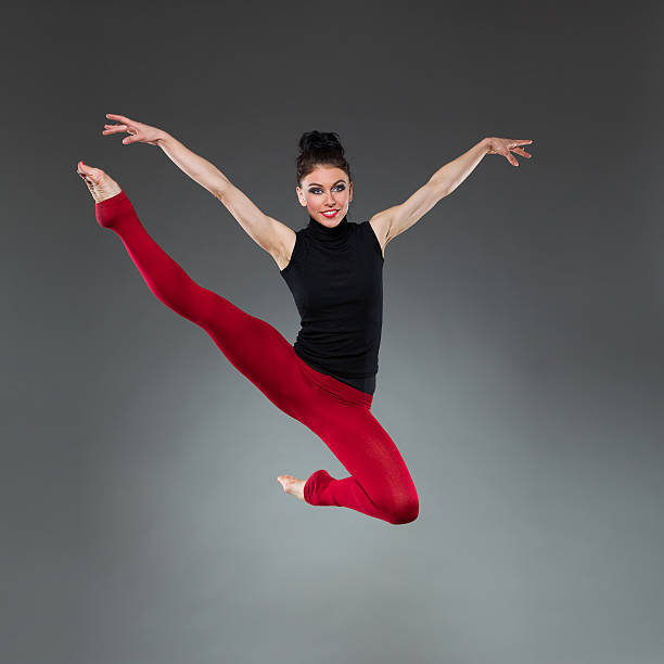 Female dancer jumping with arms outstretched. Full length studio shot on gray background